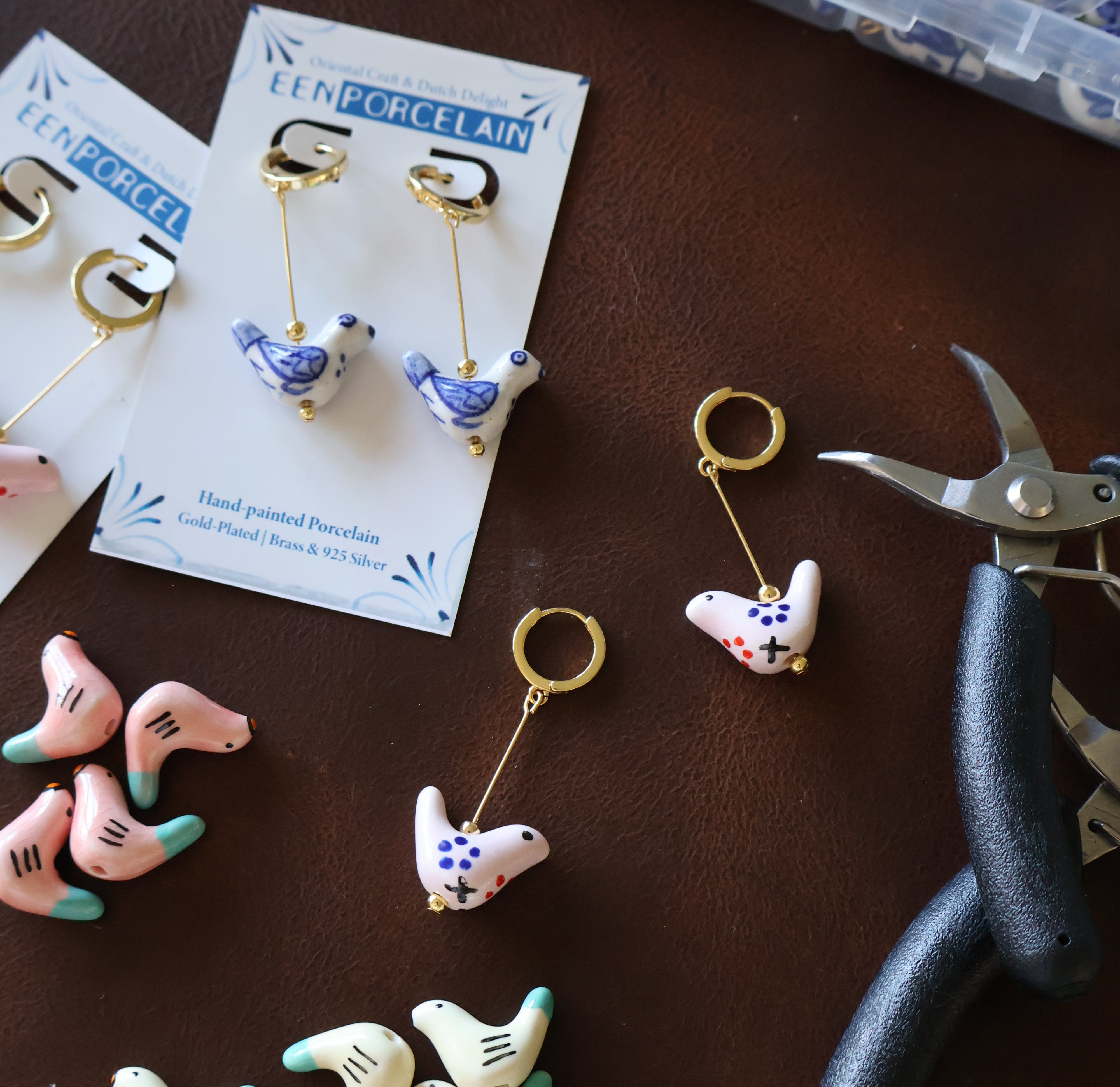 Small decorative items resembling shoes on a brown surface with pliers and packaging in the background.