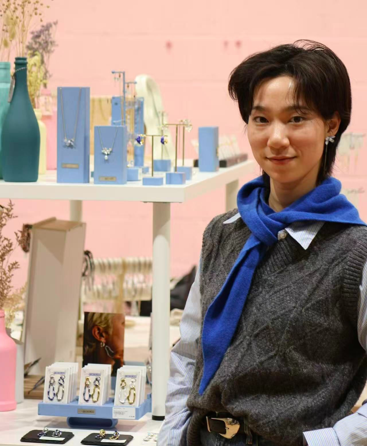 Person wearing a blue scarf in front of jewelry display